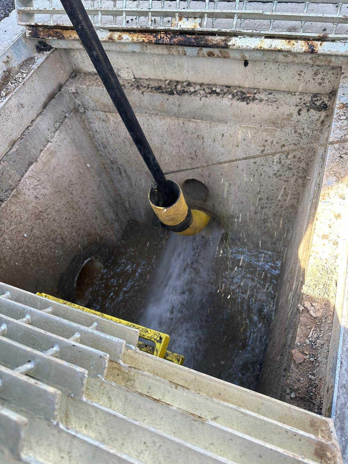 High-pressure flushing clearing sediment through a concrete drainage pit